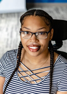 Headshot of Keisheona, a woman with light brown skin, hair braided back in two braids, wearing black framed glasses, and a navy blue and white horizontal stripe shirt.