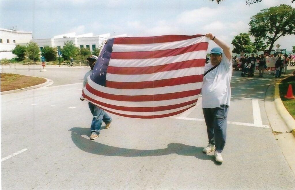 Two people holding up a large American flag with the international symbol of access made out of the stars in the flag.